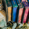 Colorful books with 'Tee Harlowe' on the spines, arranged with a candle and greenery in the background.