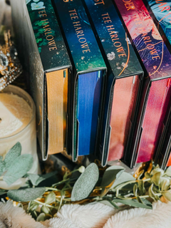 Colorful books with 'Tee Harlowe' on the spines, arranged with a candle and greenery in the background.