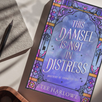 Book titled 'This Damsel is Not in Distress' by Tee Harlowe on a textured surface with a pen.